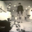 Still from Sequence 11 of Idea Demonstrations. Six spectators lie on the floor. Their shoes are removed and tied to a string which is then raised and dropped.
